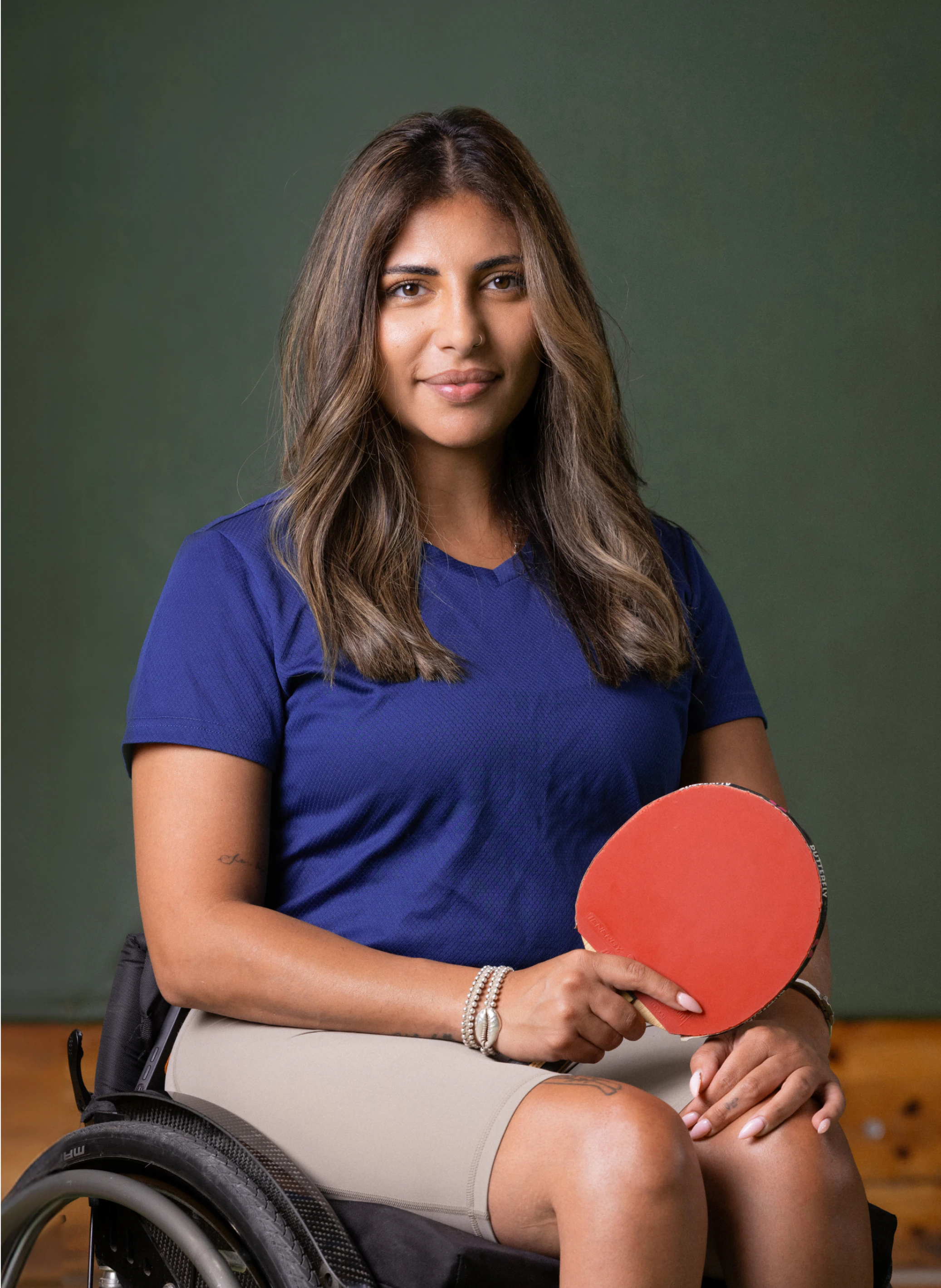 Caroline Tabib, a female athlete in a wheelchair, holding a ping pong paddle, smiling confidently. Ideal for content creators needing high-quality stock footage and sound effects for sports-related projects.