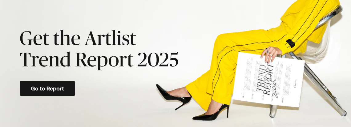 Person in bright yellow clothing sitting stylishly on a chair while holding a printed copy of the Artlist Trend Report 2025, with a call-to-action button that reads "Go to Report.